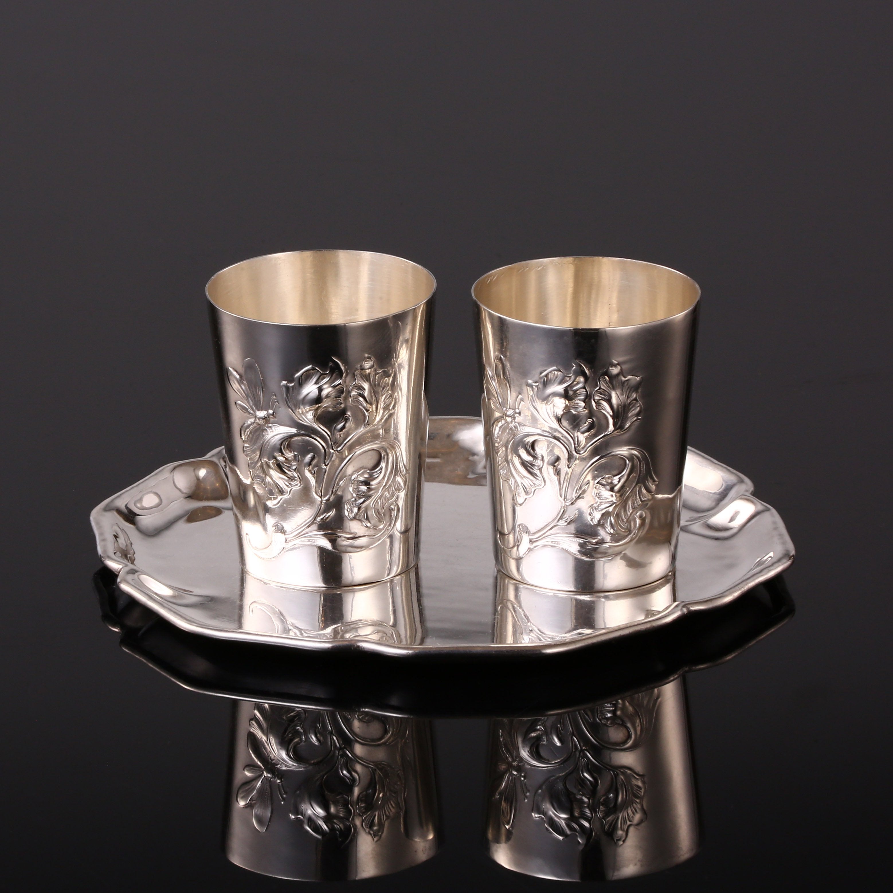 A pair of antique sterling silver wine glasses and a single antique sterling silver teacup saucer.