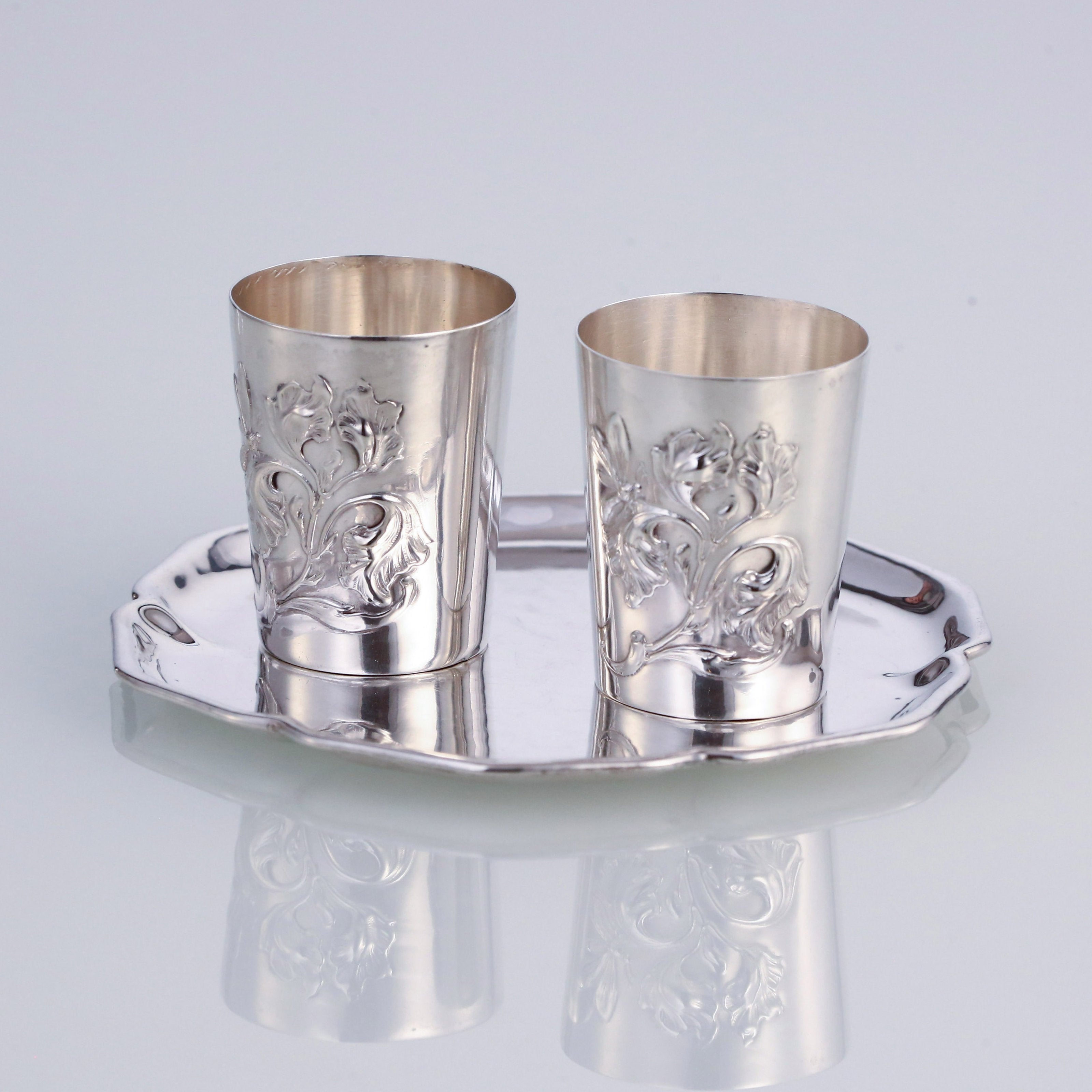 A pair of antique sterling silver wine glasses and a single antique sterling silver teacup saucer.