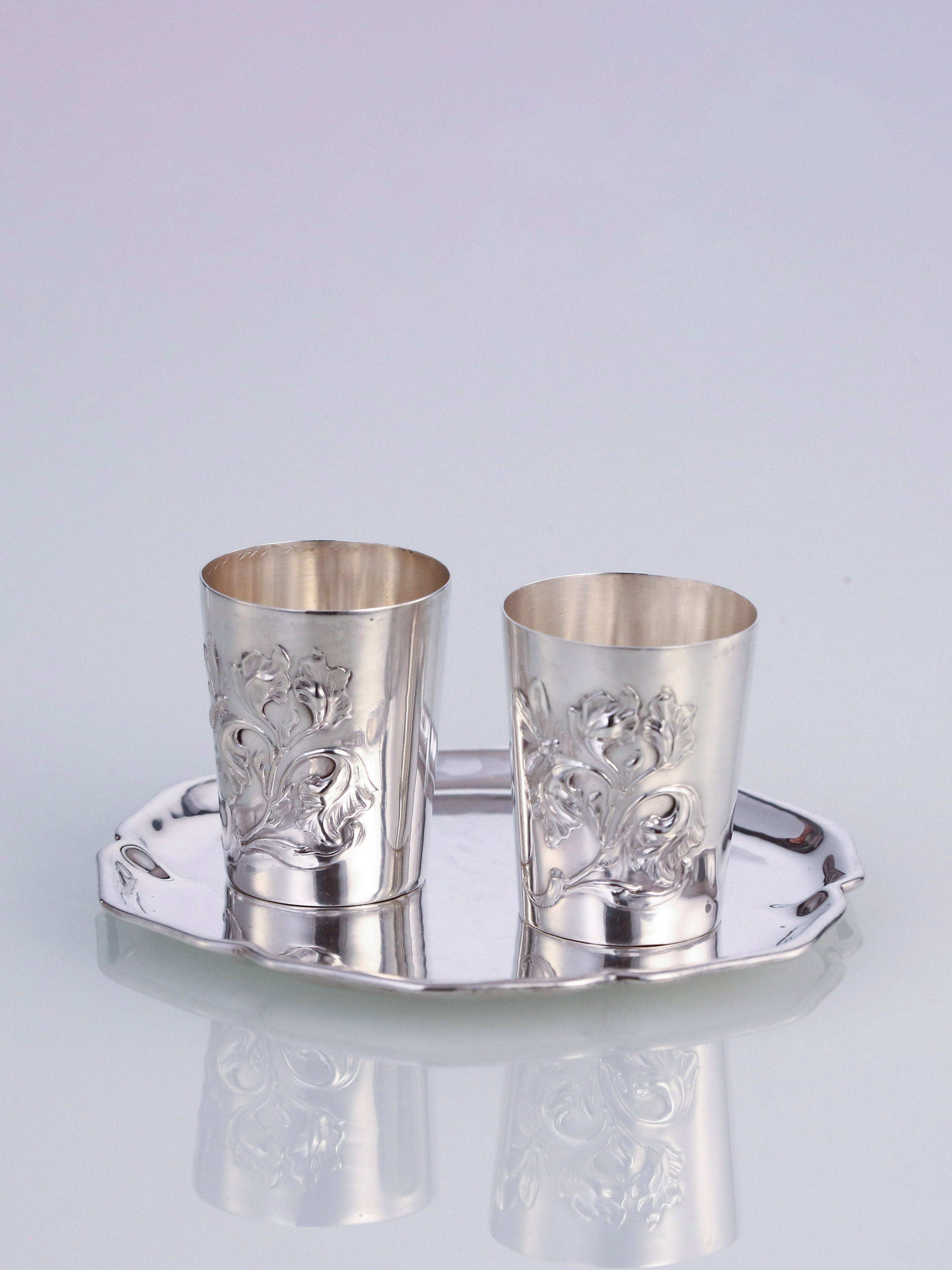 A pair of antique sterling silver wine glasses and a single antique sterling silver teacup saucer.