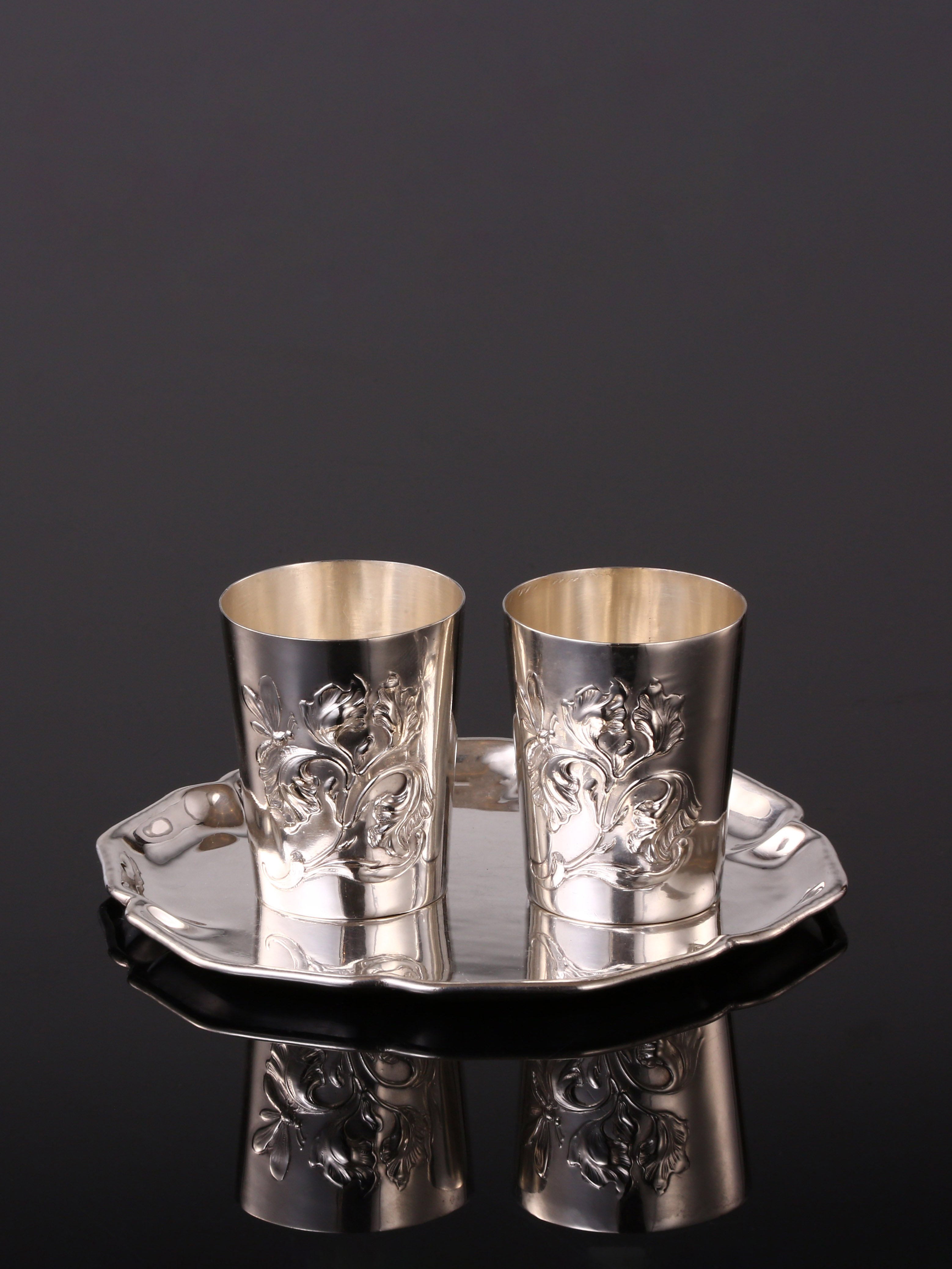A pair of antique sterling silver wine glasses and a single antique sterling silver teacup saucer.