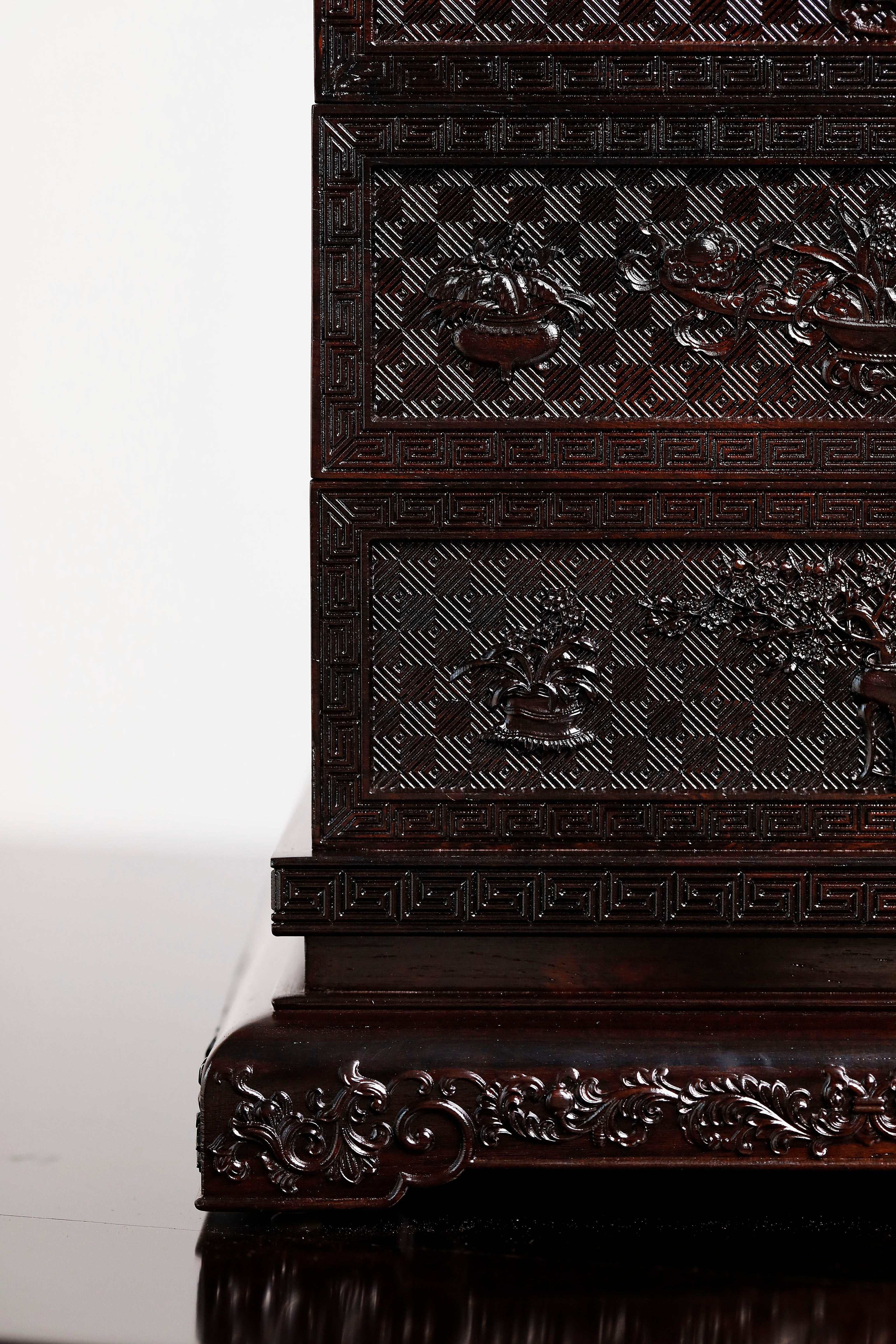 Four-tiered box in the shape of a square knot with full carvings of floral and dragon patterns.